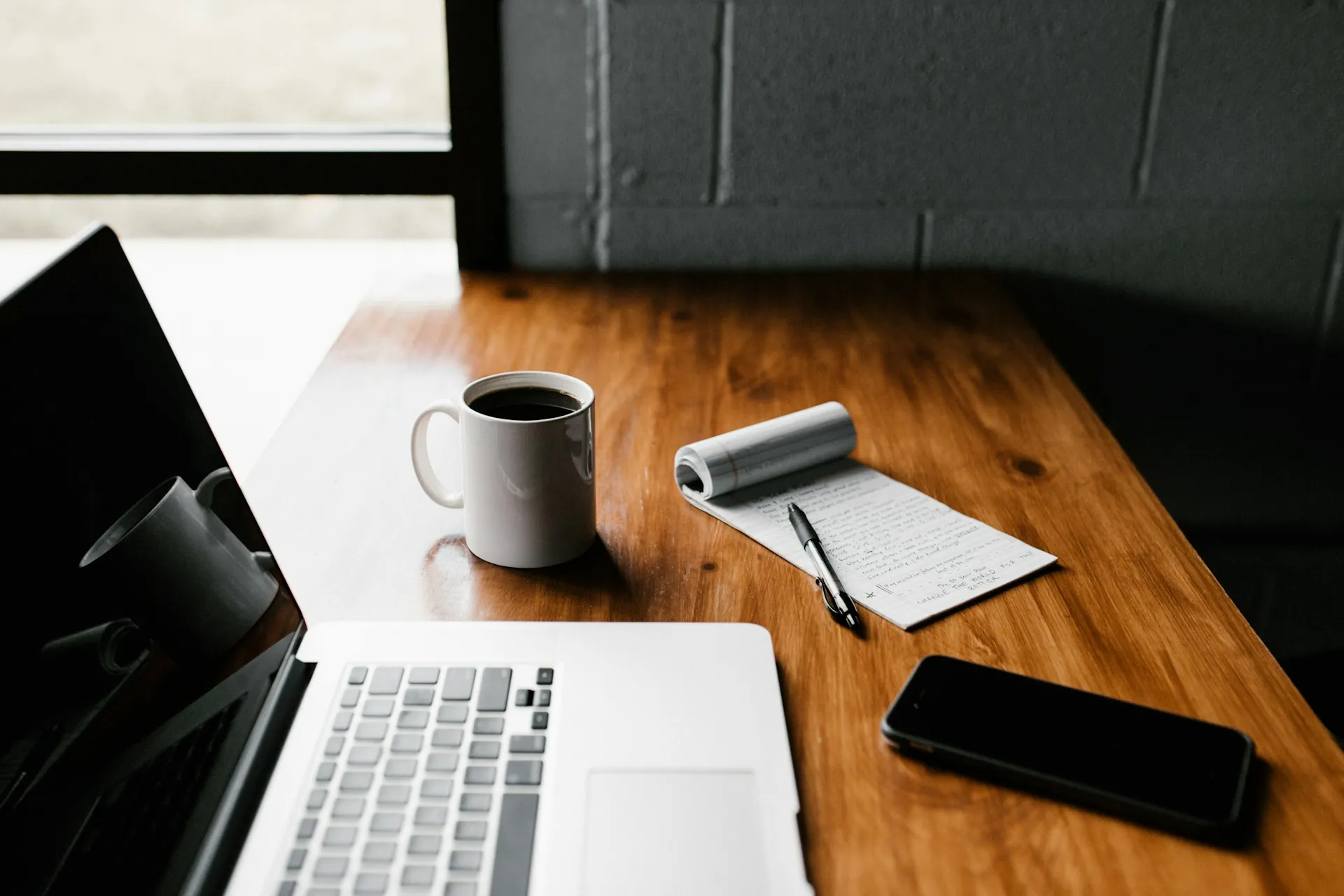 A laptop placed on a wooden table next to a cup of coffee and a phone